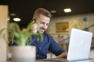 Young successful businessman talking on the phone and using laptop at cafe bar restaurant.